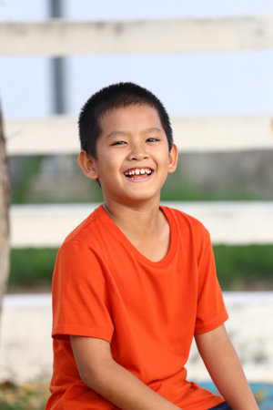 A cheerful boy wearing a bright orange shirt enjoys the outdoors. His joyful smile and carefree demeanor capture the essence of youth and happiness.の写真素材