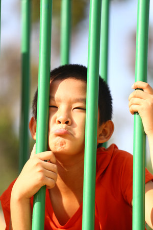 A young boy shows a funny expression while holding onto bars at a playground. This candid moment captures the joy and playfulness of childhood.の写真素材