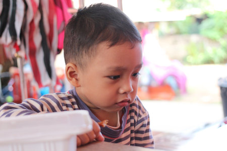 A thoughtful young boy enjoys a snack, displaying concentration and curiosity. This candid moment captures the innocence of childhood in a casual setting.の写真素材