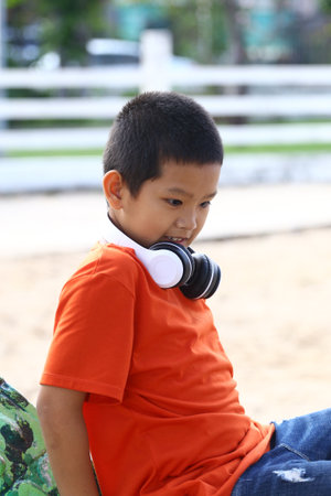A cheerful boy in a bright orange shirt is enjoying his time outdoors while wearing headphones. The scene captures his joy and focus in a casual, relaxed setting.の写真素材