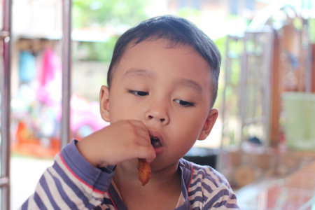 A young boy sitting indoors is enjoying a tasty snack with a focused expression. This moment captures the essence of childhood curiosity and joy during meal time.の写真素材