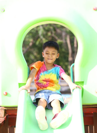 A young child in a colorful tie-dye shirt slides down a playground slide, capturing the essence of joy and fun in outdoor play on a sunny day.の写真素材