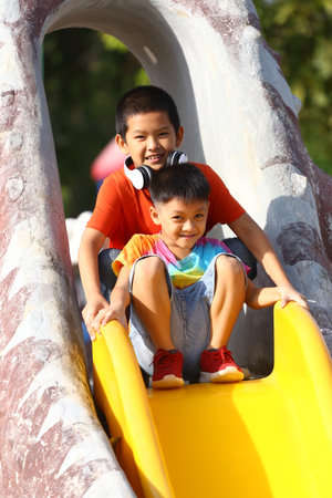 Two children are sliding down a colorful play structure in a vibrant outdoor playground, capturing the essence of joyful play and friendship in the sun.の写真素材