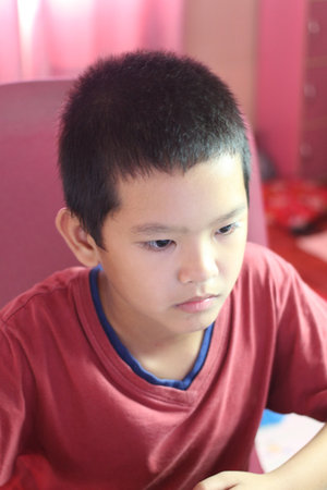 A focused boy sitting at a home desk, engaged with a computer. He displays a serious expression, highlighting concentration in a comfortable indoor setting.の写真素材