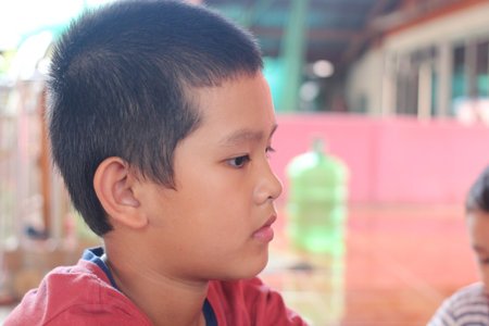 A thoughtful boy in profile, lost in contemplation. His focused expression captures the essence of childhood wonder and innocence in a colorful indoor setting.の写真素材
