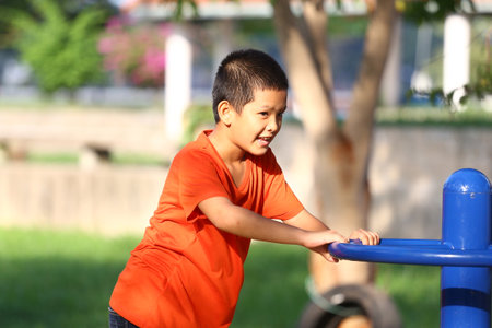 A young boy in a vibrant orange shirt enjoys playing and exercising outdoors in a park. He showcases happiness and vitality while engaging with his surroundings.の写真素材