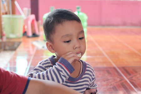 A young child sits indoors, savoring a snack with delight. The bright setting and joyful expression capture the essence of childhood moments.の写真素材