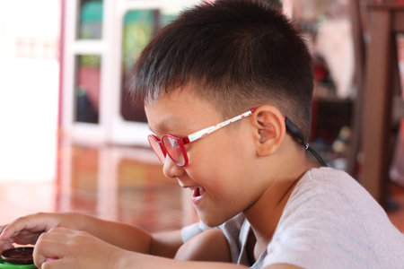 A joyful child wearing glasses enjoys a creative activity indoors. Capturing a moment of happy concentration, this image showcases the beauty of learning through play.の写真素材