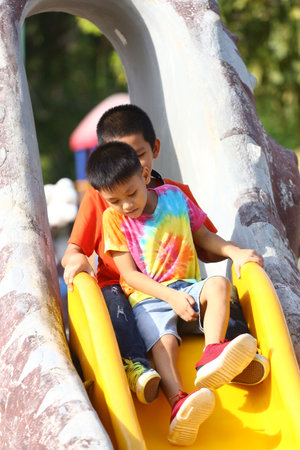 Two children share a moment of joy sliding down a bright yellow playground slide, showcasing the essence of childhood fun and adventure.の写真素材