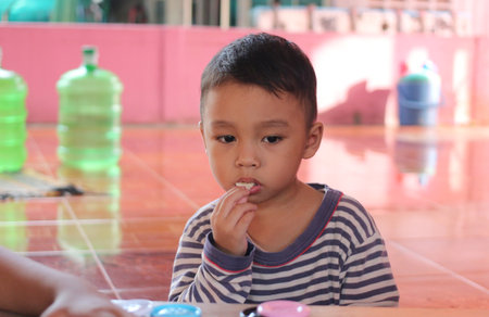 A thoughtful young boy engages thoughtfully in a playful activity, showcasing concentration and curiosity in a colorful indoor environment filled with toys.の写真素材
