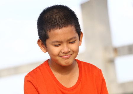 A joyful young boy with short hair wearing a bright orange shirt enjoys a moment outdoors. His cheerful expression captures the essence of carefree childhood.の写真素材