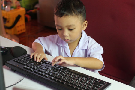 A young child intensely focused on typing on a keyboard, showcasing curiosity and engagement with technology in a home workspace setting.の写真素材