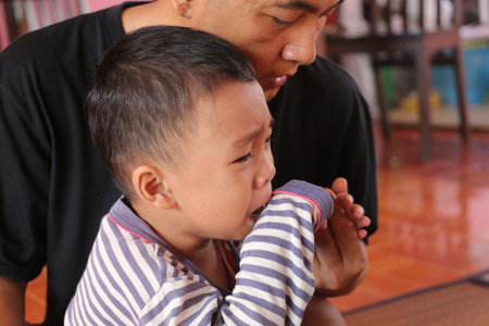 A touching moment captures a child crying while being comforted by a caregiver. The close-up reveals deep emotions and the essence of parental support.の写真素材