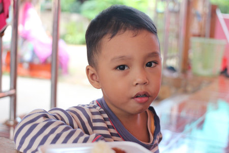 A young boy with a curious expression enjoys a meal outdoors. The scene captures the essence of childhood and innocence in a warm, inviting setting.の写真素材