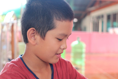 A young boy in a red shirt displays concentration while engaged in an activity. The candid moment captures childhood innocence and curiosity in a warm, inviting environment.の写真素材