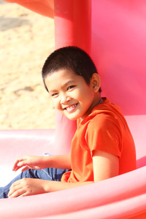 A cheerful boy enjoys a sunny day on a colorful playground slide, showcasing pure joy and the essence of childhood play and exploration in a vibrant outdoor setting.の写真素材