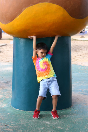 A young boy joyfully hangs from a colorful playground structure, showcasing a moment of fun and excitement in an outdoor play environment.の写真素材
