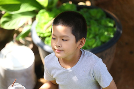 A young boy smiles gently in a lush garden, surrounded by vibrant green foliage. His expression radiates joy and innocence, capturing a tranquil moment.の写真素材