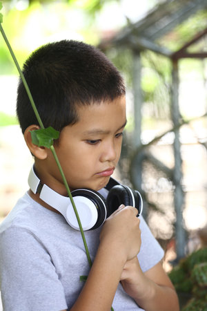 A young boy with headphones is lost in thought while surrounded by nature. The greenery and serene atmosphere create a perfect backdrop for relaxation and music enjoyment.の写真素材