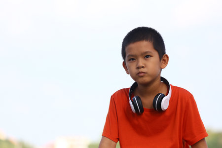 A young boy in an orange shirt and headphones is seen outdoors, looking serious and focused while...