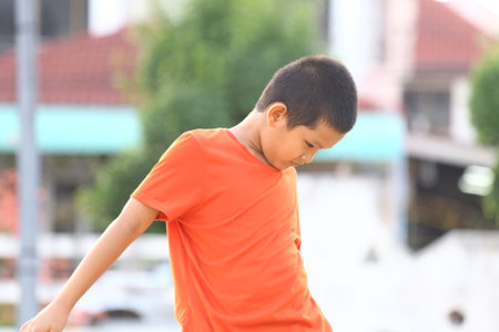 A young boy in an orange shirt enjoys outdoor play, capturing the essence of childhood joy and spontaneity on a sunny day. Perfect for themes of youth and activity.の写真素材