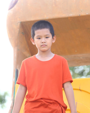 A young boy in an orange shirt stands confidently at a playground, embracing the joy of play while basking in the warm sunlight. Perfect for capturing childhood innocence.の写真素材