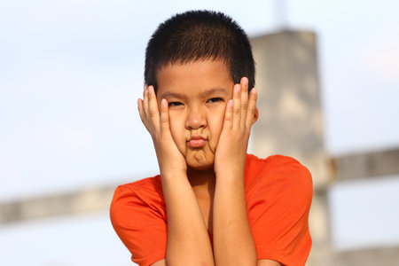 A young boy expresses displeasure with a playful pout, contrasting against a bright outdoor background. Perfect for themes of childhood emotions and expressions.の写真素材