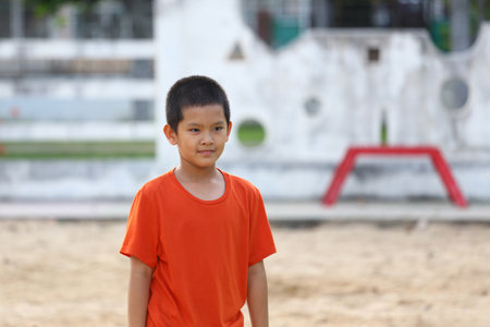 A young boy in an orange shirt enjoys playtime at an outdoor playground. His cheerful expression captures the essence of childhood joy and active exploration in a sunny environment.の写真素材