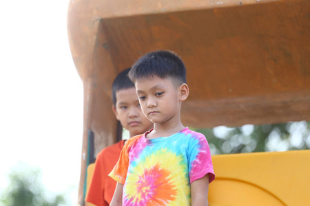 Two children are captured in a candid moment, one showing a thoughtful expression while wearing a colorful shirt. The scene reflects youth and friendship.の写真素材