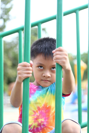 A young boy in a colorful tie-dye shirt plays at the playground, holding onto the bars with a determined expression, embodying youthful joy and curiosity.の写真素材