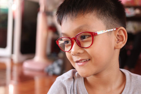 A cheerful boy wearing colorful glasses smiles warmly in a cozy indoor environment, capturing the essence of childhood joy and curiosity in a playful moment.の写真素材