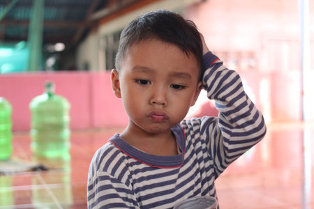 A thoughtful child appears lost in contemplation, capturing a moment of innocence and curiosity in a casual indoor setting, evoking deep emotions.の写真素材