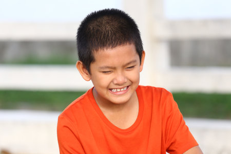 A joyful boy in a bright orange shirt smiles broadly, showcasing his youthful innocence and contagious happiness in an outdoor setting.の写真素材