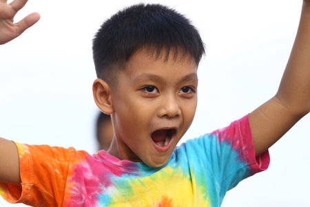 A joyful boy celebrating outdoors, wearing a bright tie-dye shirt. His expression radiates excitement and energy, capturing the essence of childhood joy.の写真素材