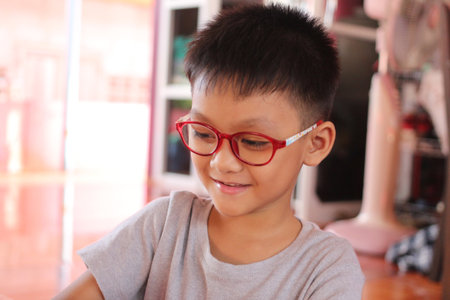 A young boy with red glasses smiles while engaging in activities at home. The cheerful atmosphere captures the essence of childhood joy and innocence.の写真素材