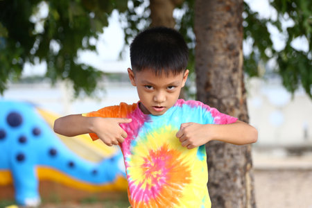A confident boy in a colorful tie-dye shirt stands outdoors. His expressive pose captures youthful energy and playful spirit, surrounded by nature.の写真素材