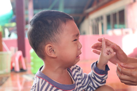 A young boy expresses sadness while a caring hand gestures toward him, capturing a moment of emotional connection and support in an indoor setting.の写真素材