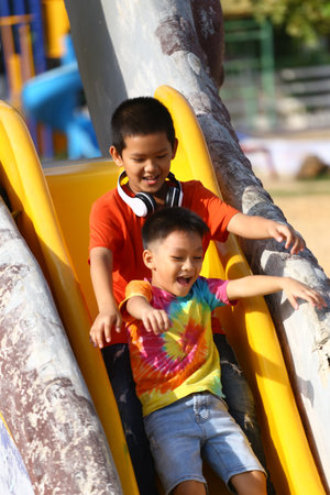 Two joyful children slide down a bright yellow slide in a playground, showcasing their excitement and laughter while enjoying a sunny outdoor day.の写真素材