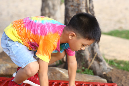 A joyful child wearing a colorful tie-dye shirt plays outdoors. The boy climbs on playground equipment, showcasing his carefree spirit and summer happiness.の写真素材