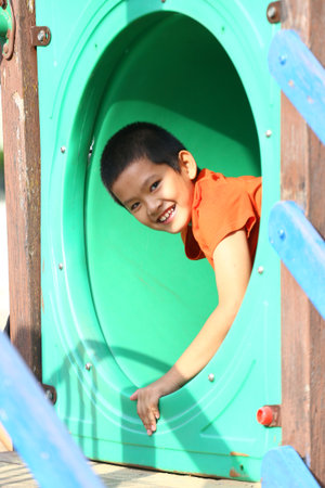 A joyful child with a big smile enjoys playing in an outdoor playground slide. The scene captures happiness and carefree moments in a colorful setting.の写真素材
