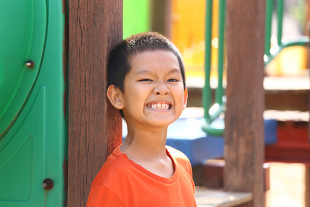 A cheerful boy smiles broadly while enjoying time at a colorful playground. His vibrant orange shirt contrasts with the lively background, capturing pure joy.の写真素材