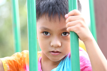 This image captures an intense moment of a child on playground equipment. The vibrant colors and direct expression evoke curiosity and youthful energy.の写真素材