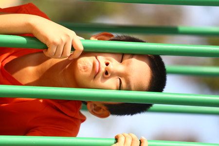 A young boy joyfully plays on vibrant green playground equipment, expressing happiness and energy under the warm sun, capturing the essence of childhood adventure.の写真素材