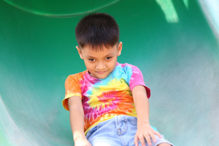A cheerful child enjoys the thrill of sliding down a playground slide. The sunny day and vibrant shirt enhance the playful atmosphere of outdoor fun.の写真素材