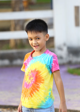 A joyful child wearing a vibrant tie-dye shirt smiles while playing outdoors. The colorful attire adds charm to a bright, sunny day in the park.の写真素材