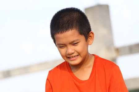 A joyful boy wearing a bright orange shirt smiles in the sunlight. This candid moment captures childhood happiness and carefree outdoor play.の写真素材