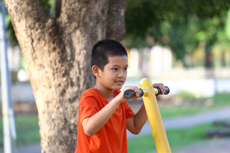 A young boy in an orange shirt engages in playful exercise at a park, showcasing joy and determination while enjoying the outdoors in a vibrant setting.の写真素材
