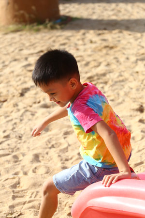 A joyful child in a colorful shirt plays on playground equipment in a sandy area. The scene captures the excitement and innocence of childhood outdoors.の写真素材