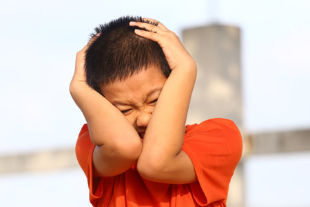A young boy displays strong emotion by covering his ears and grimacing. This evocative portrait captures moments of distress and childhood vulnerability.の写真素材