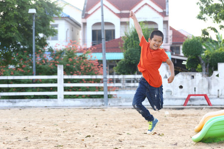 A joyful boy wearing an orange shirt is jumping in an outdoor setting, capturing the essence of childhood and playfulness with bright colors and a fun atmosphere.の写真素材